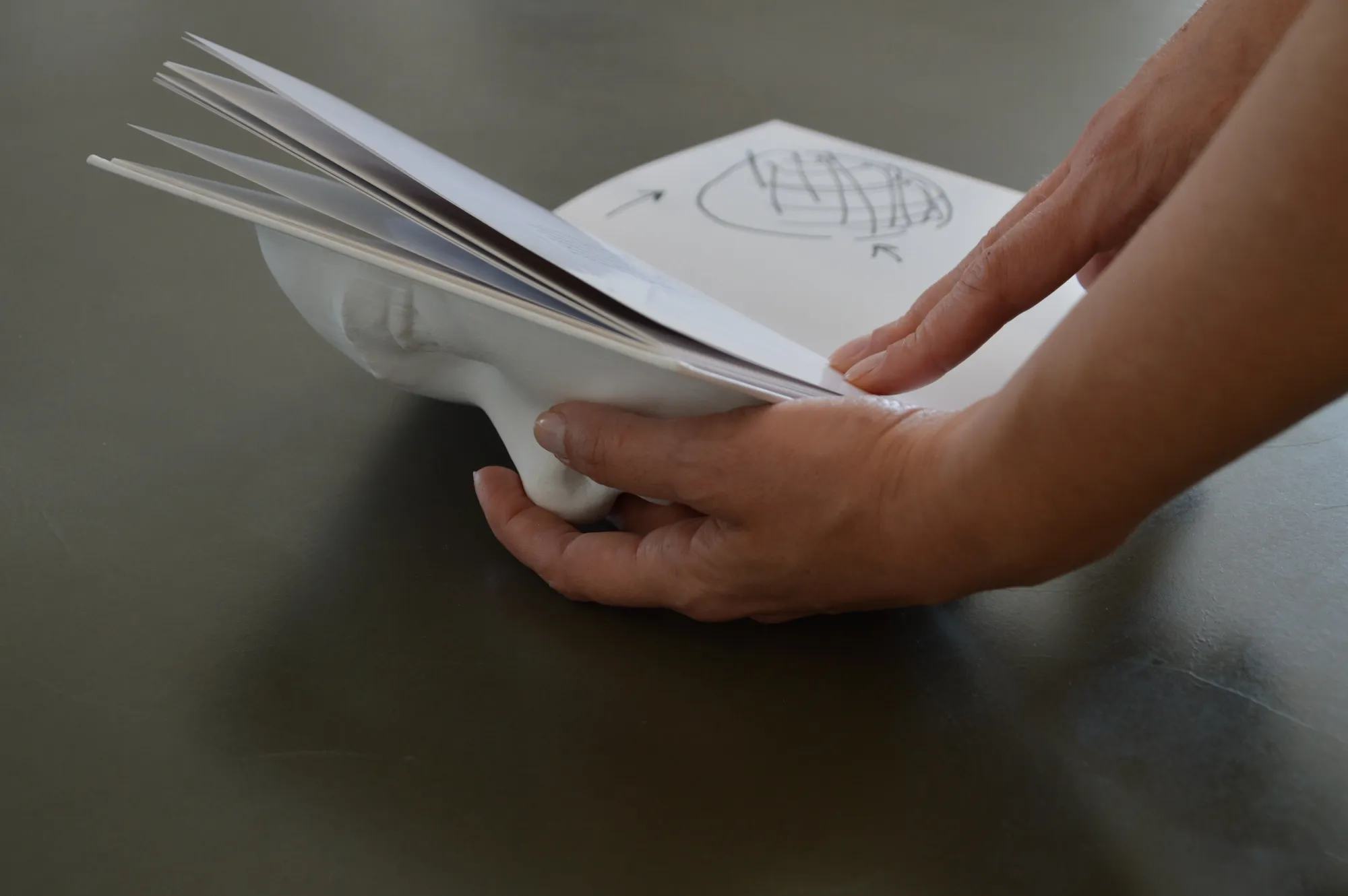 The 3D-printed face-shaped object with the book's pages fanned out beneath it.