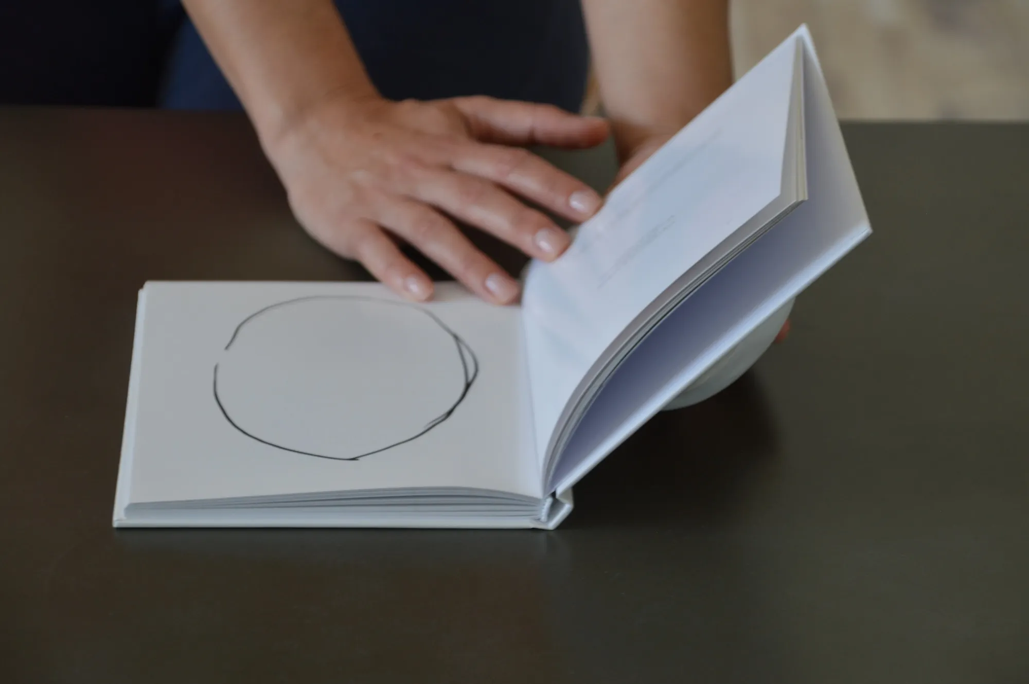 A hand beside an open book page with a plain hand-drawn circle.
