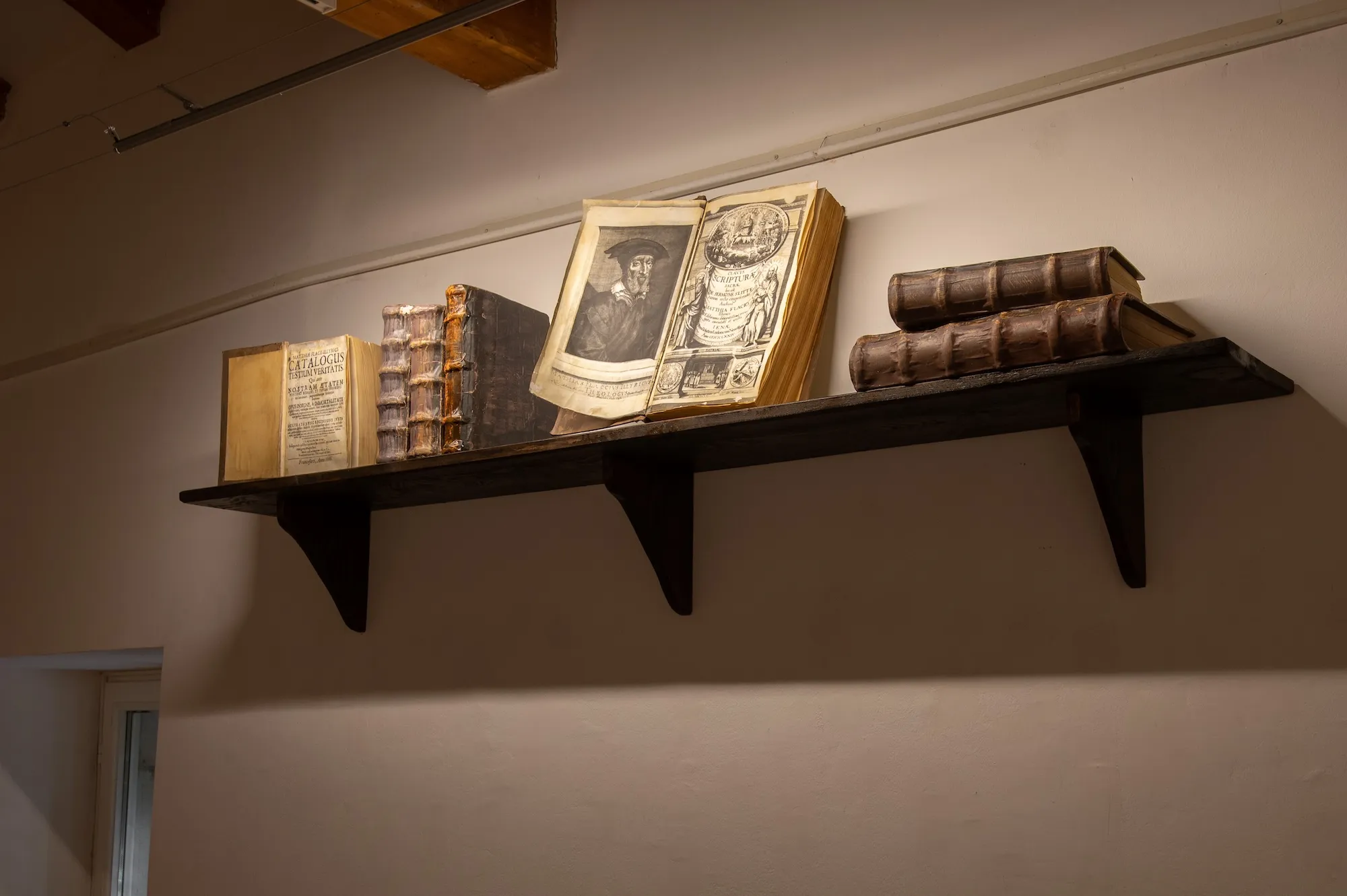 Close-up of the wall shelf holding antique books by Matija Vlačić Ilirik, including an open volume with an engraved portrait.