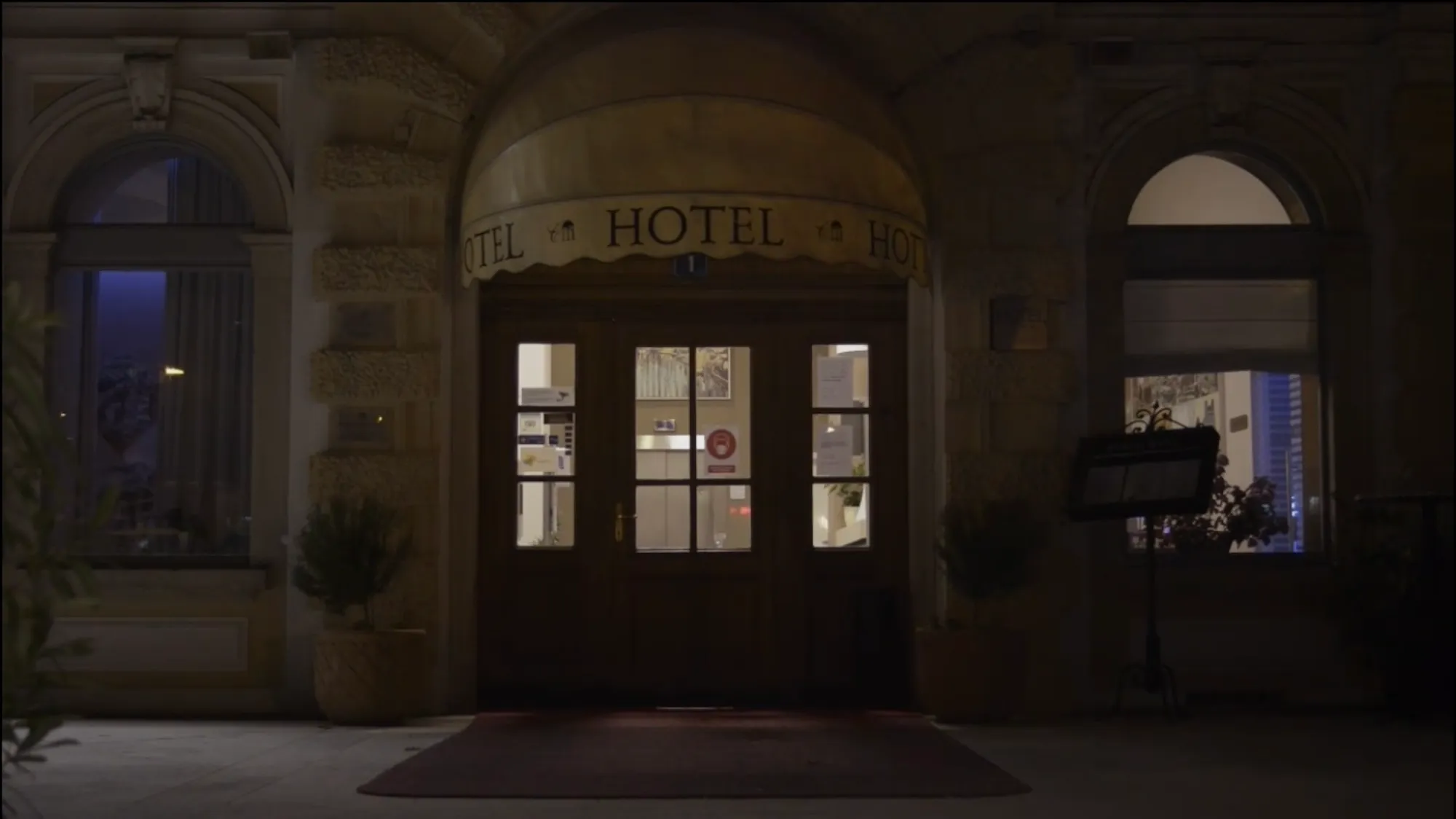 Close-up of the hotel's entrance at night, with "HOTEL" repeated across the scalloped awning.