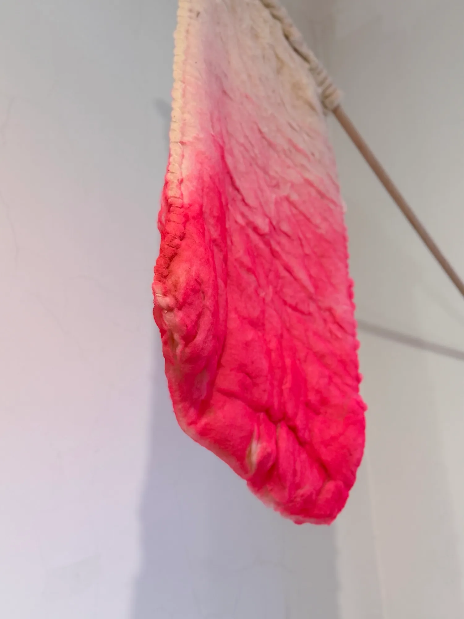Close-up of a felted wool flag on a stick, dyed in a white-to-pink ombré gradient.