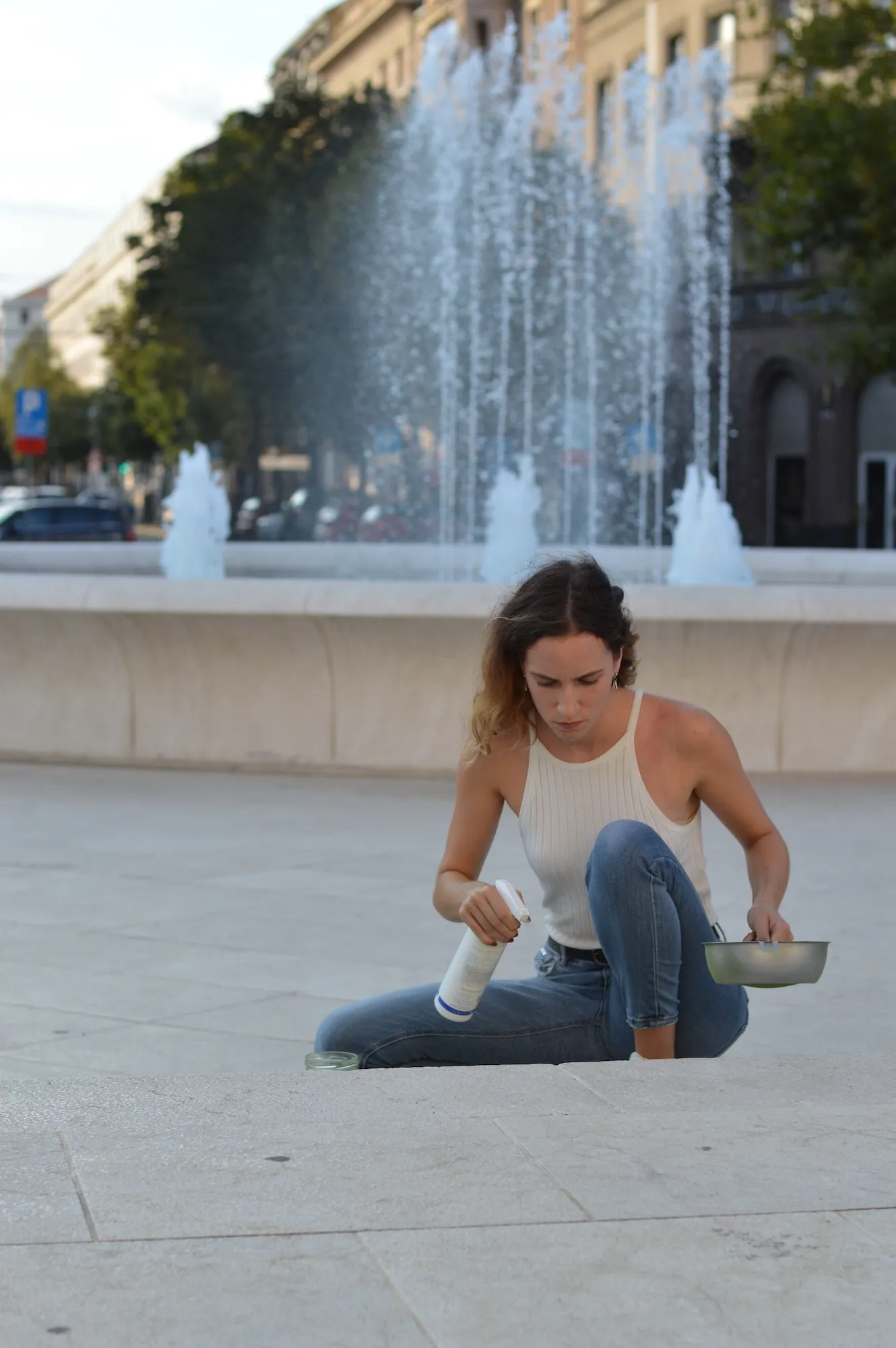 Wide view of a city square with a fountain, the artist crouching to apply powder to a strip of pavement.