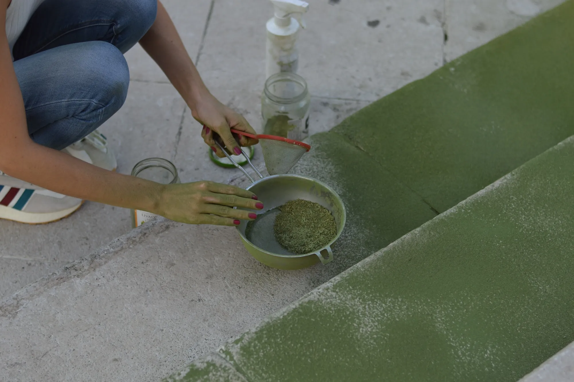 Two people's legs stepping over the green line of powder on the pavement.