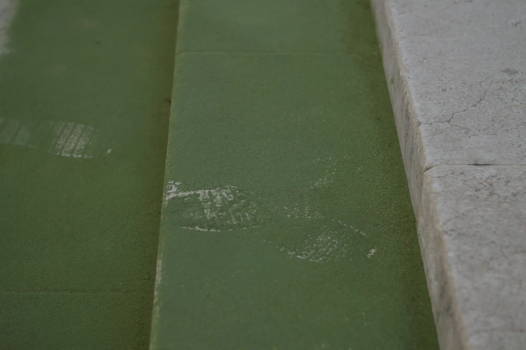 Close-up of the green powder line on the pavement, showing overlapping footprints.