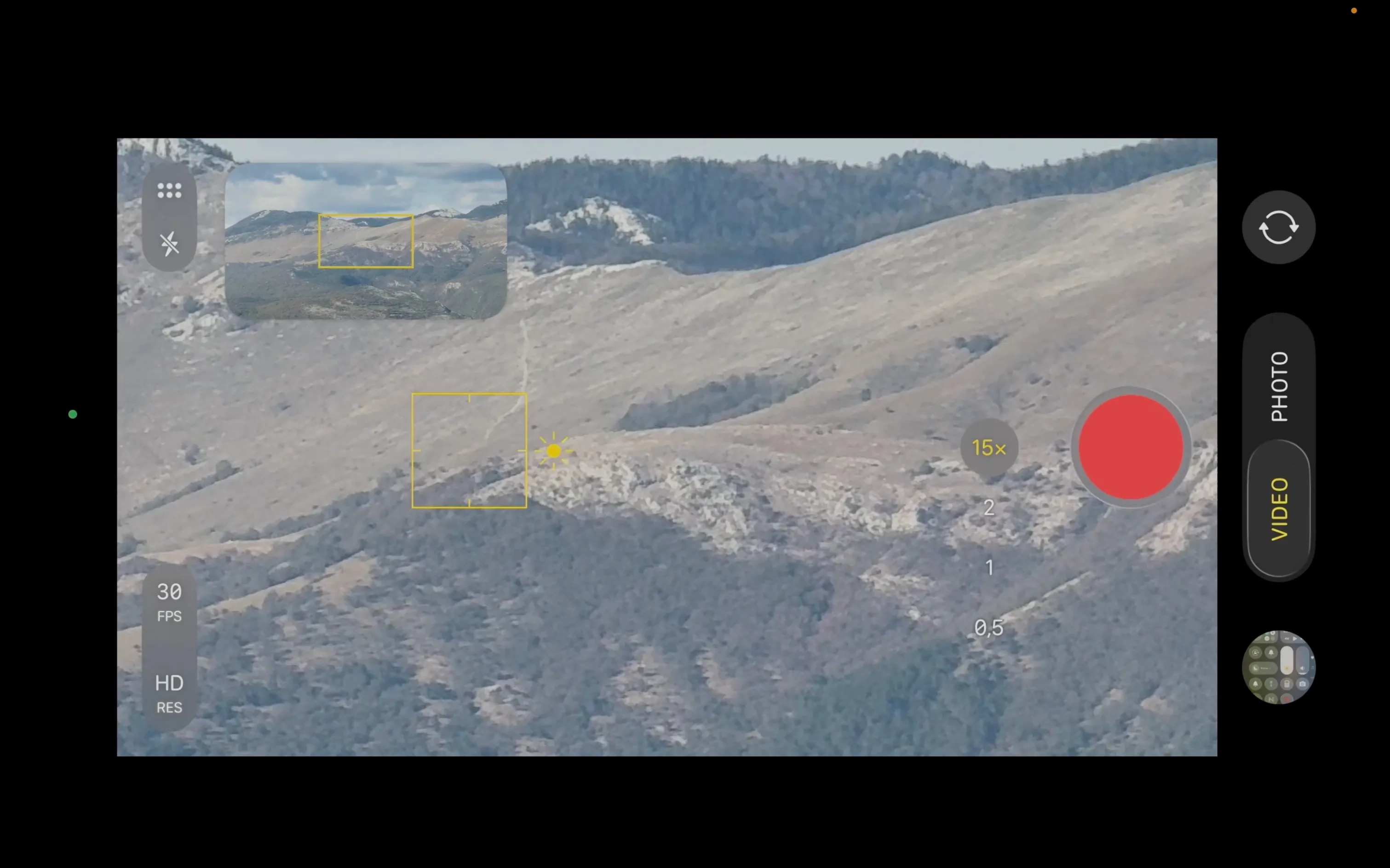 A screen-recorded phone camera interface at 15× zoom, showing a grainy, magnified hillside of grass, scrub, and limestone, with a small overview of the whole mountainside in the corner.