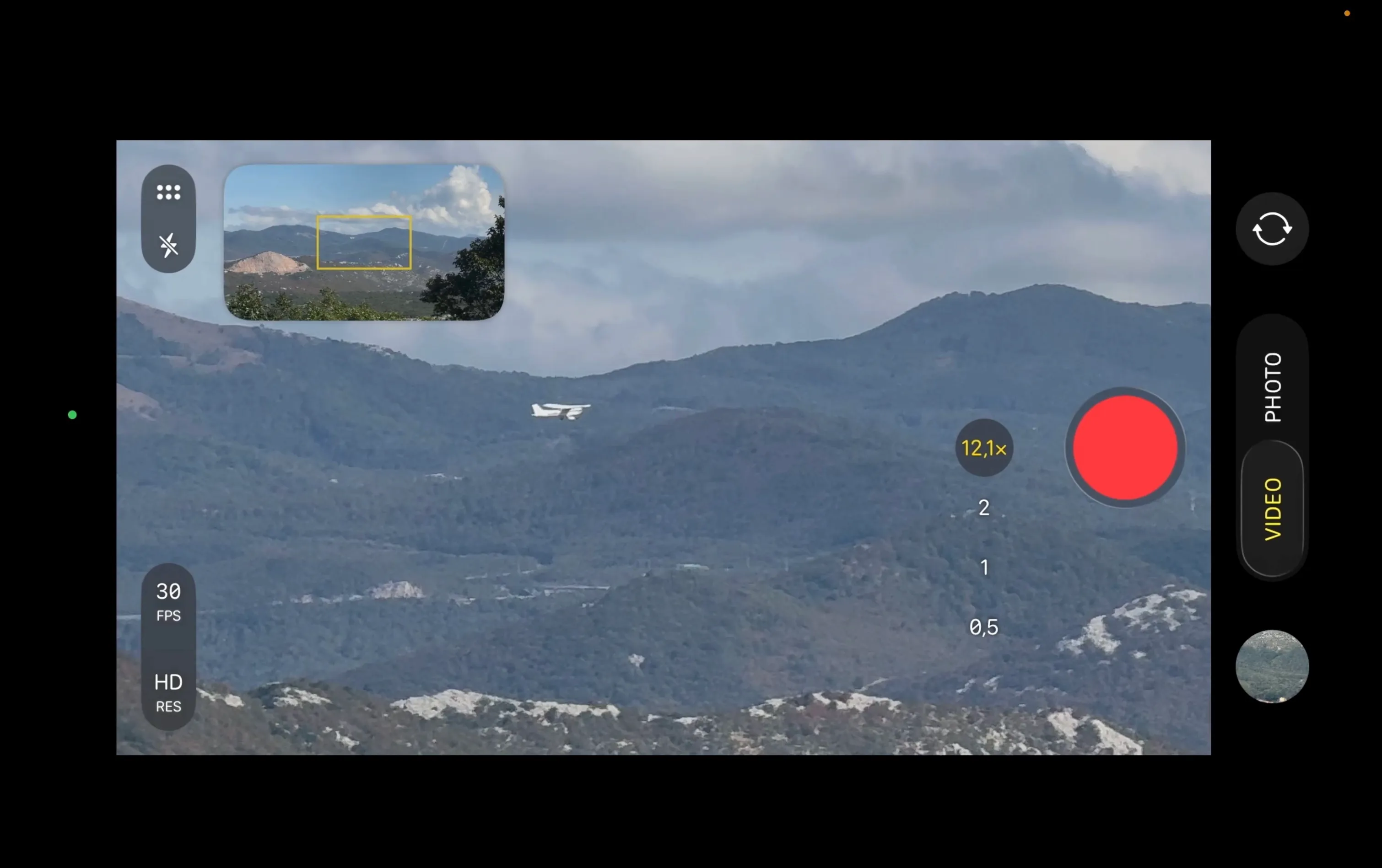 A screen-recorded phone camera interface at 12.1× zoom, showing a small white propeller plane flying over forested hills, with a quarry visible in the overview inset.