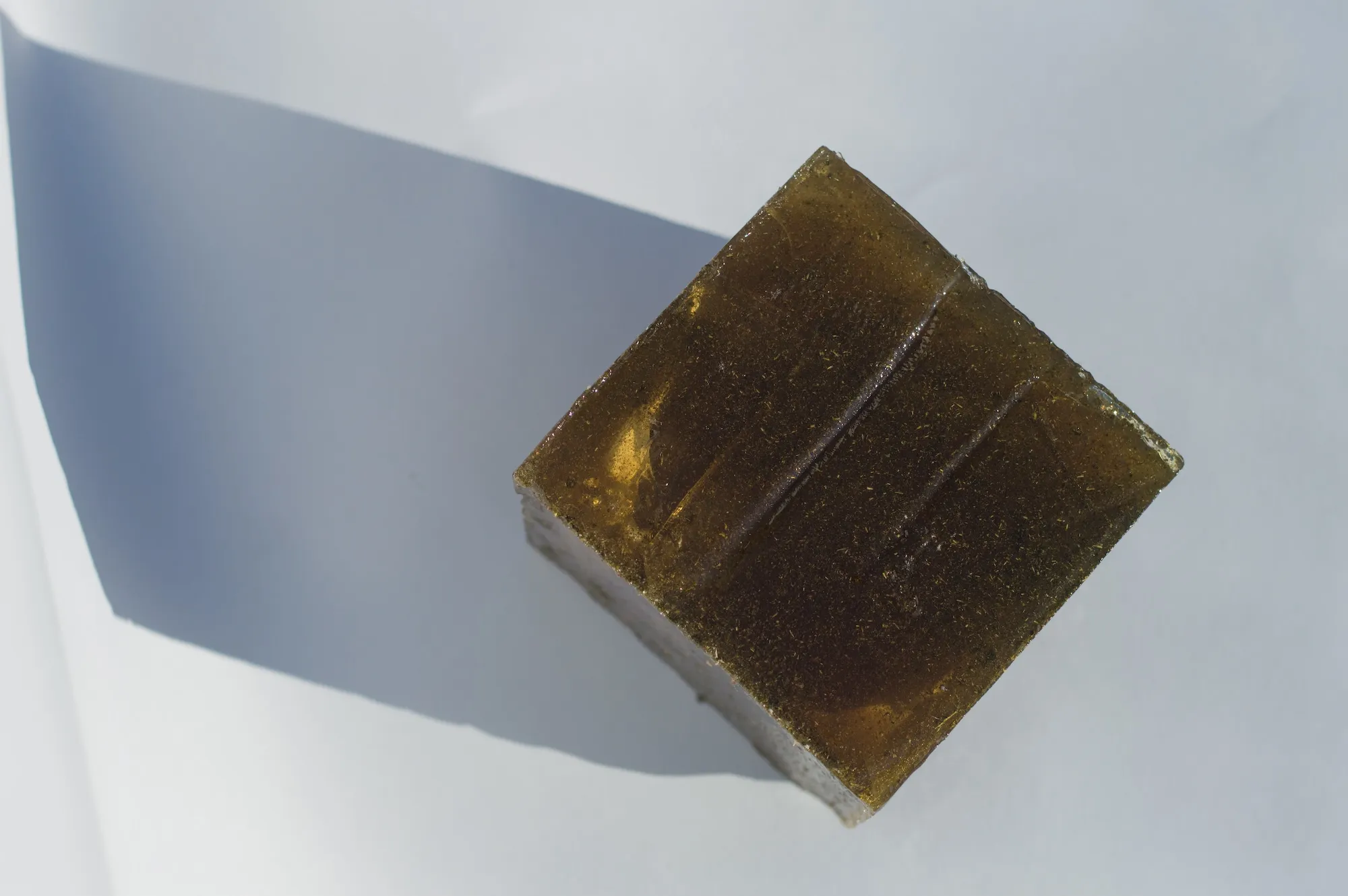 Diagonal overhead view of the amber isomalt cube against a light blue backdrop.