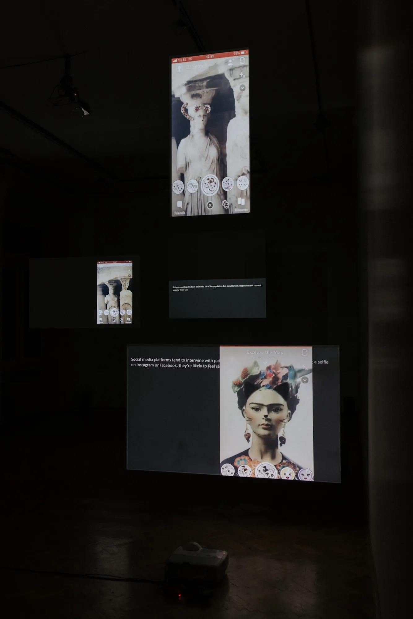 Installation view: projected screens showing Snapchat filters over classical female statues from art history, including a bust wearing a Frida Kahlo-style filter, beside wall text about body dysmorphia statistics.