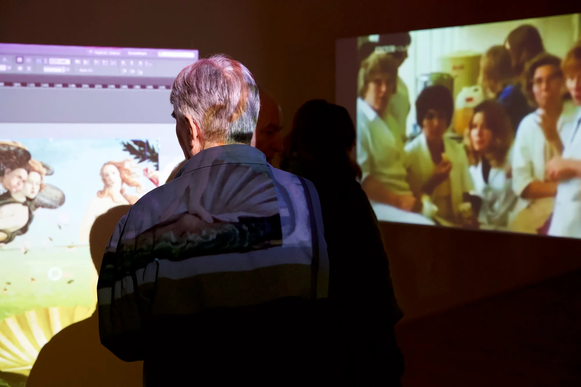 Installation view: projected screens showing video-editing software alongside a Renaissance painting and archival footage of a group of people.