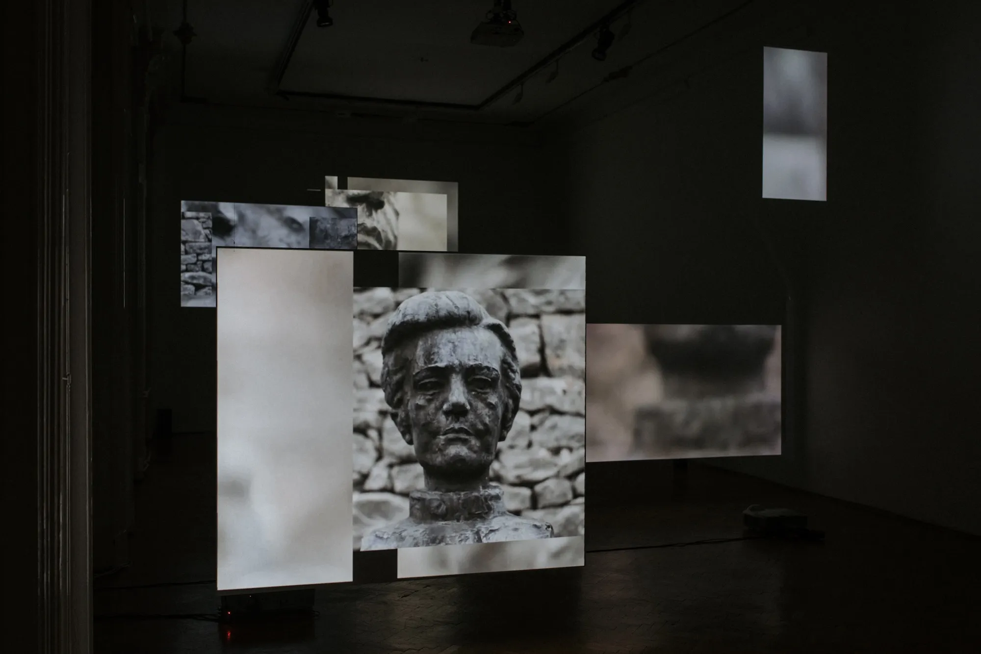 Installation view: multichannel screens showing close-ups of a bronze bust against a stone wall texture.