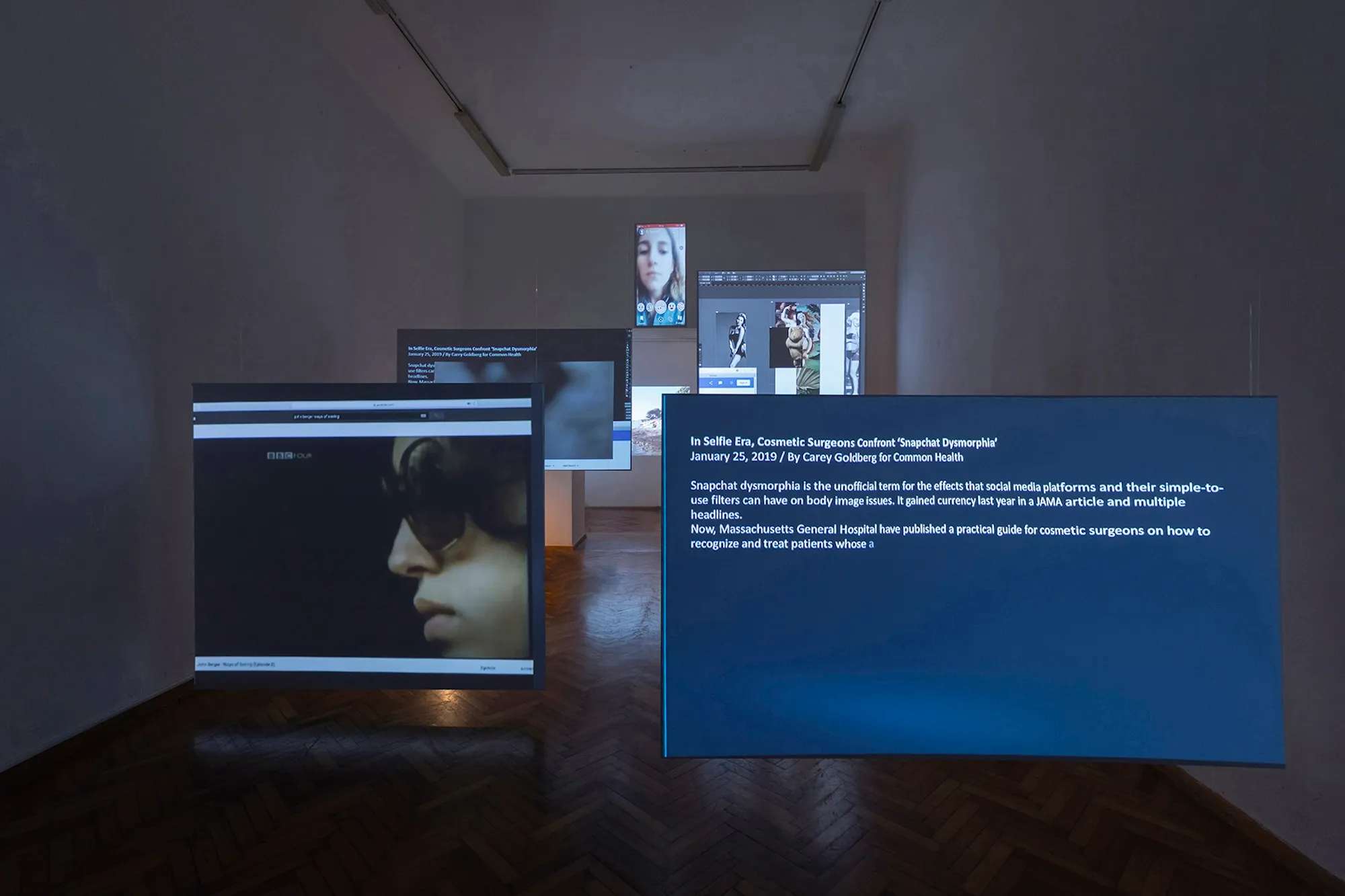 Installation view: a large screen displaying the article 'In Selfie Era, Cosmetic Surgeons Confront Snapchat Dysmorphia' in full, beside a Snapchat filter selfie and a photo collage.