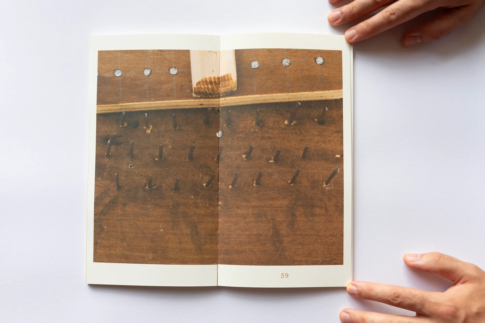 An open spread of the book showing a close-up photograph of a wooden pegboard tool used for wool processing.