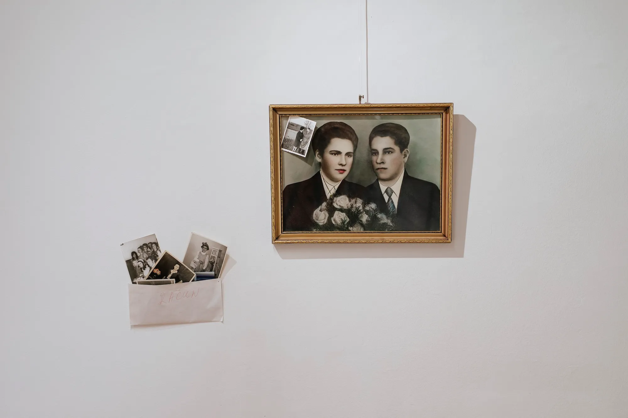 A framed wedding portrait on the gallery wall, beside an envelope holding a small stack of family photographs.