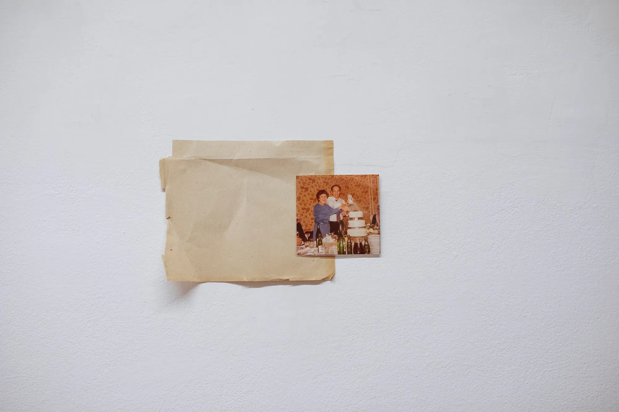 A faded photograph of a couple cutting a wedding cake, taped to the gallery wall.