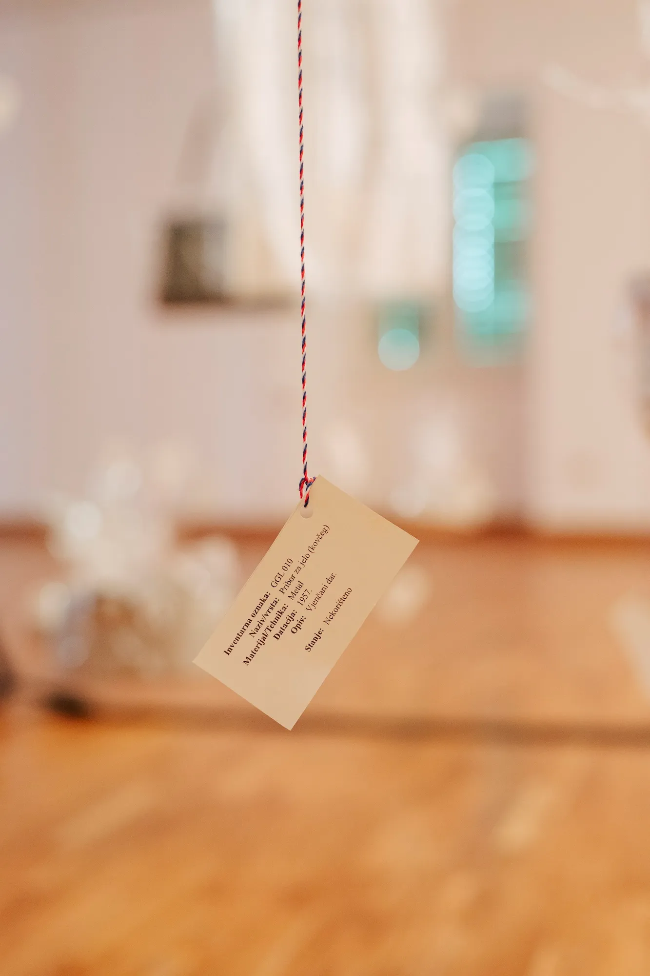 Close-up of a handwritten inventory tag hanging from a string, listing the object's material, date, and donor description.