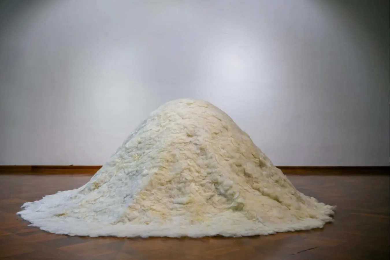 A large mound of white felted wool against a plain gallery wall.